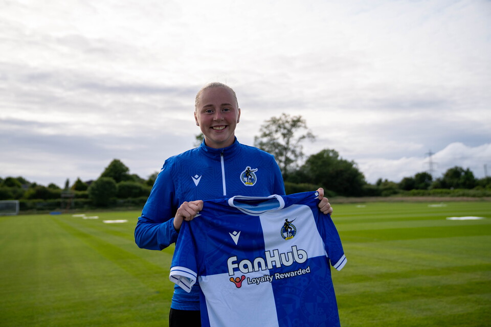 Erin Bloomfield holding a Bristol Rovers Shirt on a football pitch.