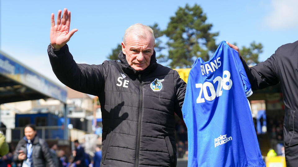 Steve Evans holding a shirt after signing his contract to stay with the club
